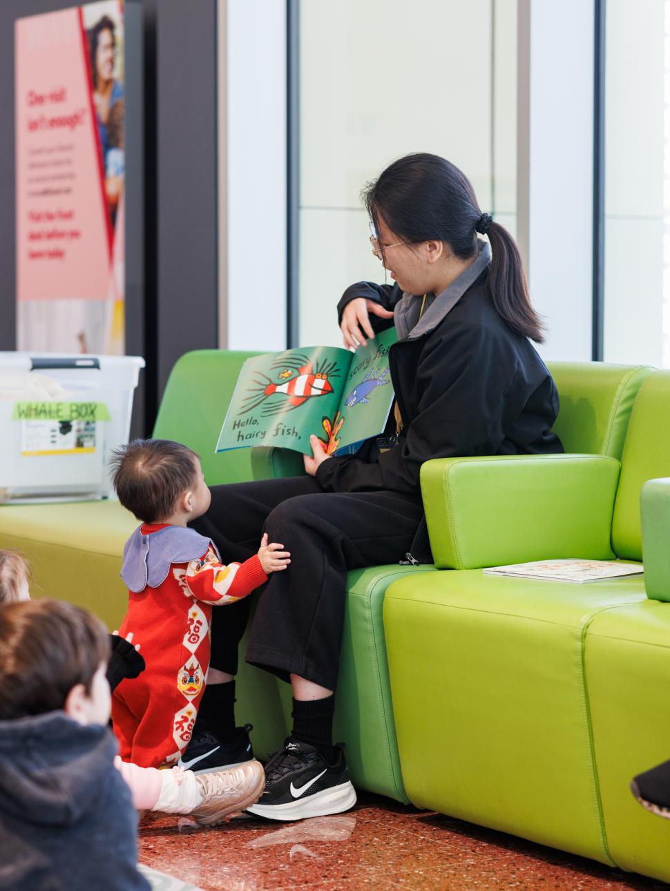 Volunteer reading a book about fish with a child at her knees looking at the book