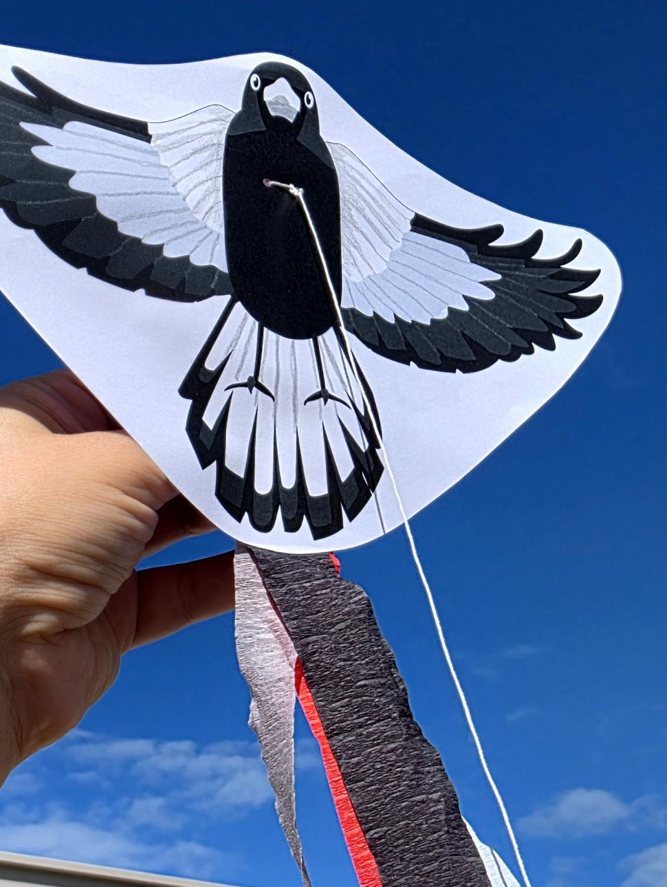 A hand holding up a kulbardi/magpie kite craft activity with a blue sky background, available at Fremantle WA Day celebrations in 2026. 