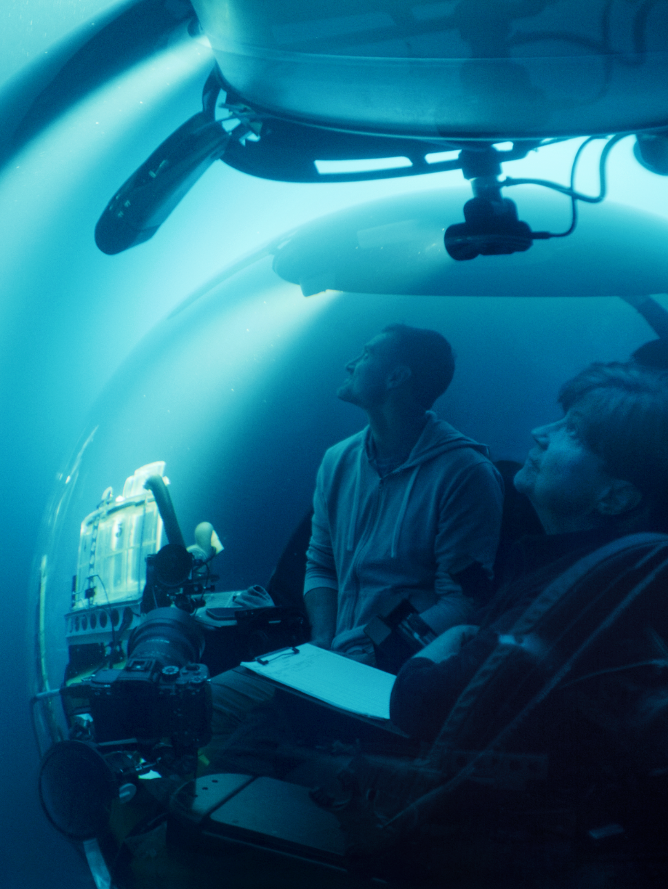 Two pepole in a submersible underwater with a camera
