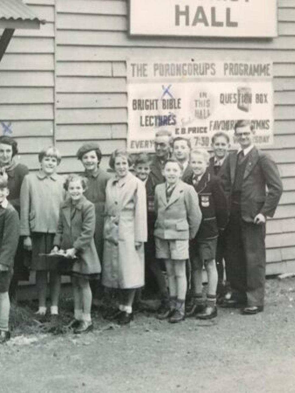 a group of people including children line up outside a hall 