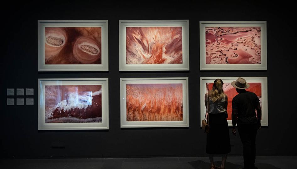 Two people stand looking at six large scale aerial photographs in a gallery