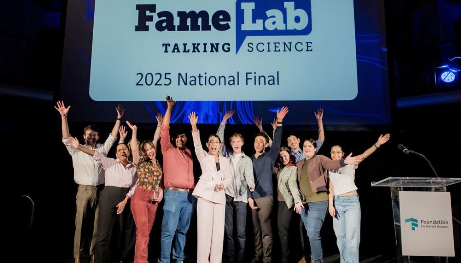 A group of people celebrating on stage, with a large screen displaying the word FameLab behind them.