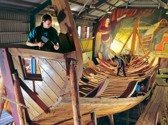 Three men using traditional hand tools to build the framework of a ship