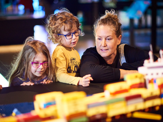 2 children and an adult looking closely at ships made of Lego.