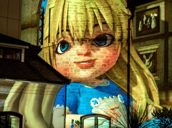 A projection of Alice in Wonderland sits smiling on the Old Gaol bricks