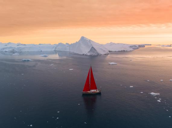 boat with red sails is sailing in water with icebergs in the background