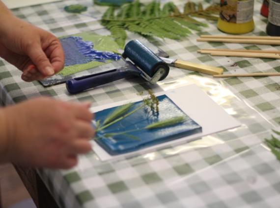 Gell plate on white paper with leaves on stop and a paint roller on the left
