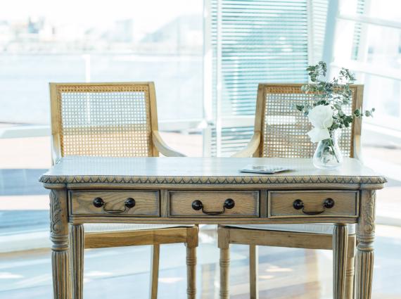 Two wicker chairs in front of a vintage-style table with a large, well-lit window in the background