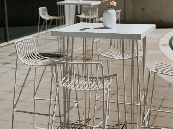 Thin-wired, high-legged chairs beside a table with pink flowers in a white vase, on the balcony of the Maritime Museum