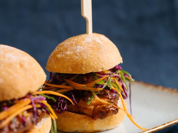 Two small sliders with a wooden skewer with shredded carrot and cabbage and a piece of golden chicken breast