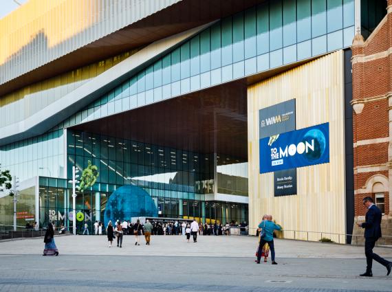 A wide shot of the ramped access to the WA Museum for wayfinding, showing the large gold and glass building decorated with 'To the Moon' exhibition content. 