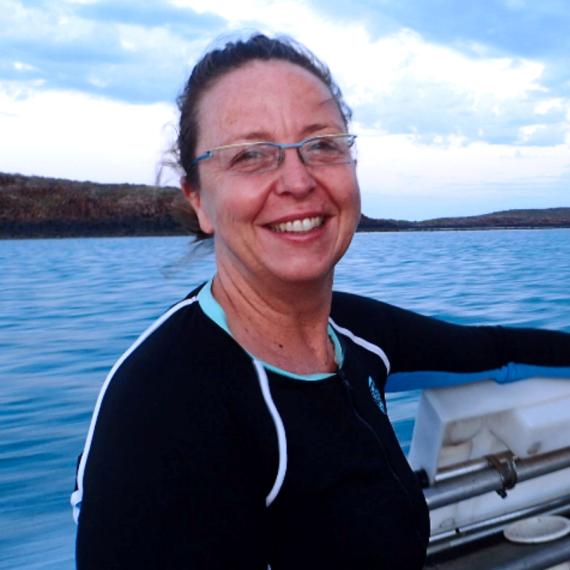 A lady in a wetsuit on a boat, smiling.