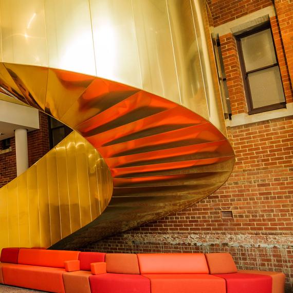 A golden spiral staircase winds upwards in front of a brick wall