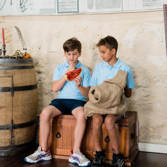 Two children sit on a wooden chest, examining an object they have pulled from a sack