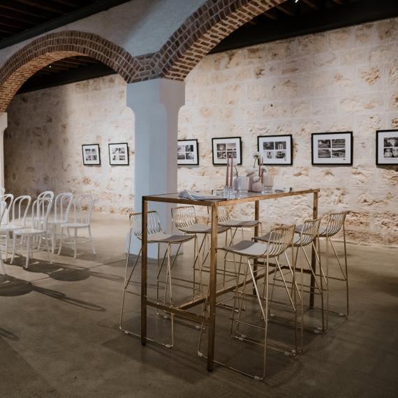 Chairs and tables are arranged for a wedding in a large room with limestone walls and an arched ceiling