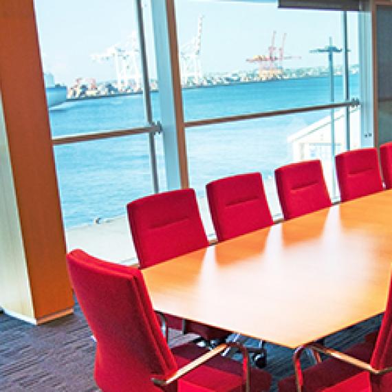 A boardroom overlooking the ocean, with red plush chairs and a large wooden table