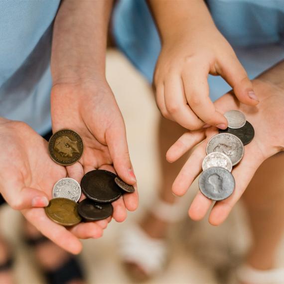 A close-up view of two children's hands holding old coins