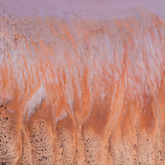 An aerial view of a hilly striated salt lake landscape in shades of red, yellow and white