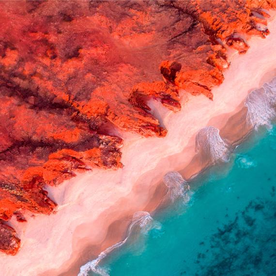An aerial view of red cliffs beside a clear turquoise sea