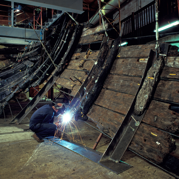 A person wearing protective equipment welding support structures onto an old shipwreck.