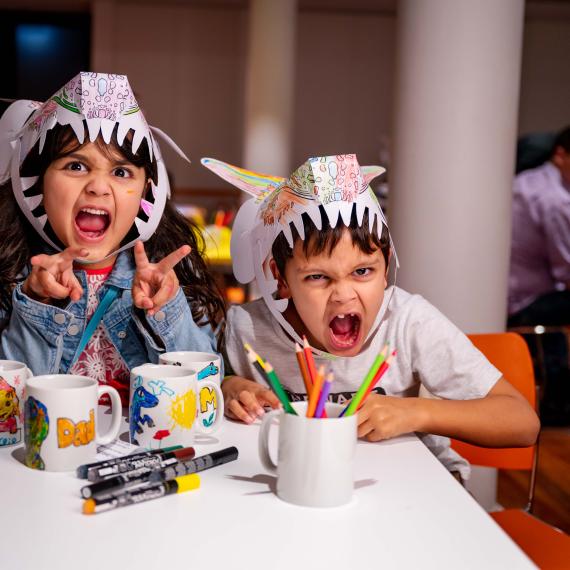 Image of two children roaring at the camera wearing paper dinosaur hats