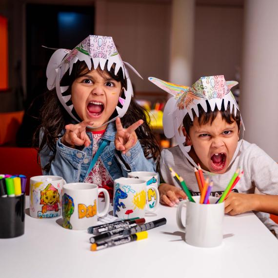 Image of two children roaring at the camera wearing paper dinosaur hats