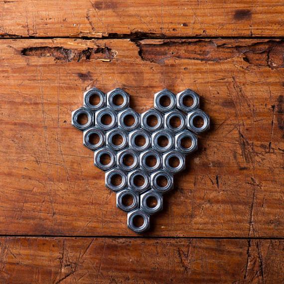 Metal nut bolts shaped in a heart positioned on a wooden board. 