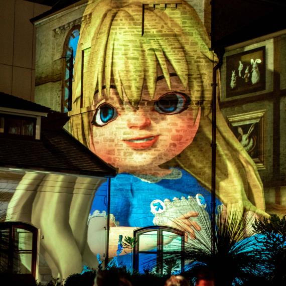 A projection of Alice in Wonderland sits smiling on the Old Gaol bricks