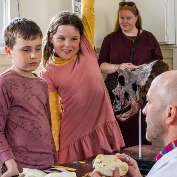 Image of kids in a classroom setting, looking at a skeleton skull being held by a teacher.
