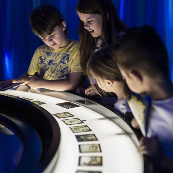 A group of children stare at a curved table top covered in photos