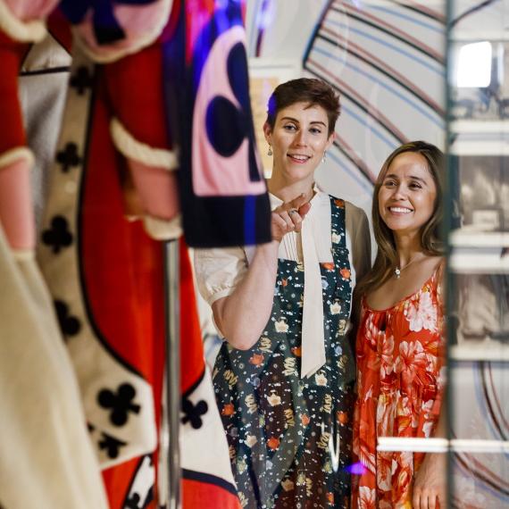 Two persons look through the protective museum glass at a large and colourful costume 