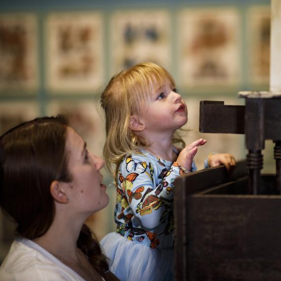 Small child is looking up over their hands at a prop with a parent nearby