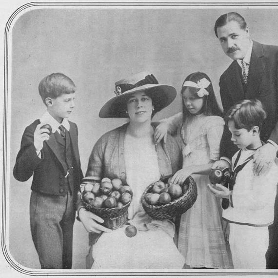 A black and white image of Clare Butt wearing a white vintage dress and hat posing with her family