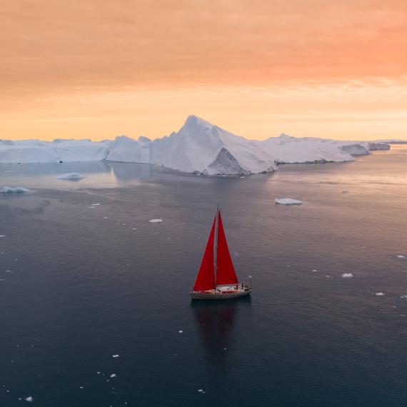 boat with red sails is sailing in water with icebergs in the background