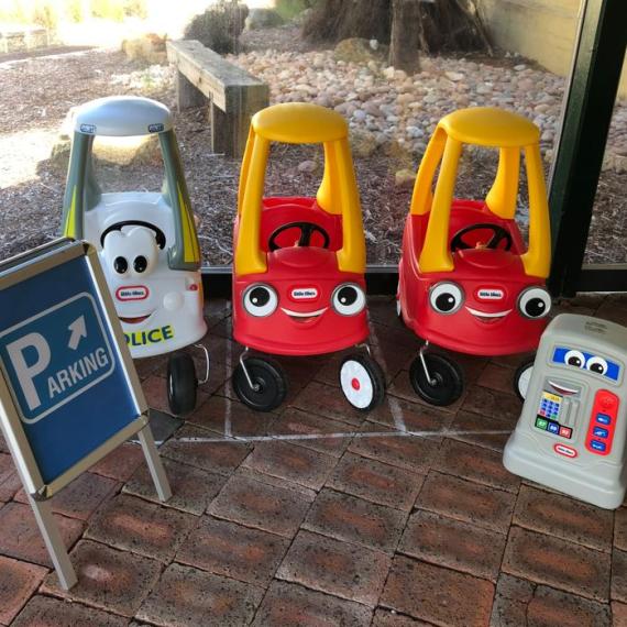 Three clasic kids cars parked alongside two traffic signs 
