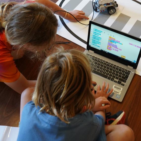 Image shows two children siting on the floor using a laptop computer to code a robotcoding 