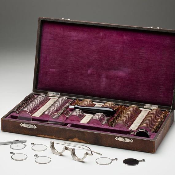a wodden case with velvet linig. box contains slots filled with eyeglasses lenses and other instuments