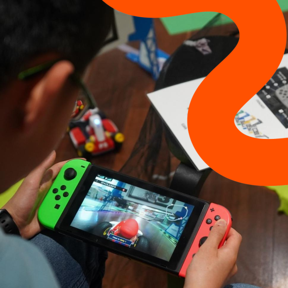  A child joyfully grips a game controller, immersed in a Mario Kart race, while an orange squiggle line adds a playful touch as a feature.