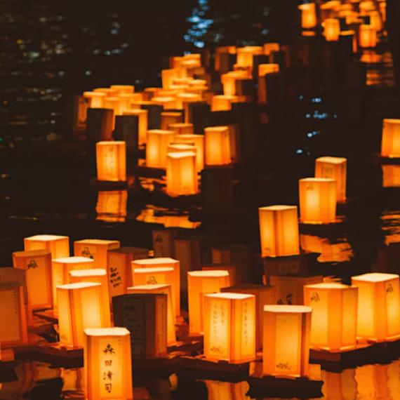 collection of rectangular paper box shaped lanterns glow as they float on water in the night all glowing 