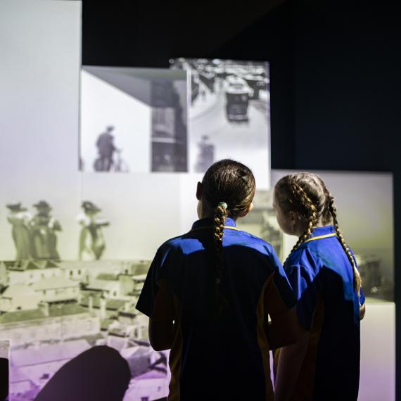 Two girls stand with their backs turned to the camera, with projections of old photos in front of them 