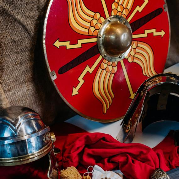 Red and gold Roman armor and helmet sits against a brown fabric background