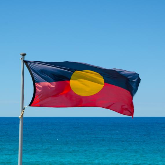 The Aboriginal and Torres Strait Islander flag flies against a bright blue sky
