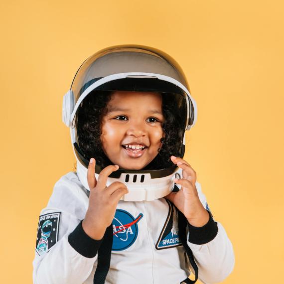 a young child smiles and has a space suit and helmet on