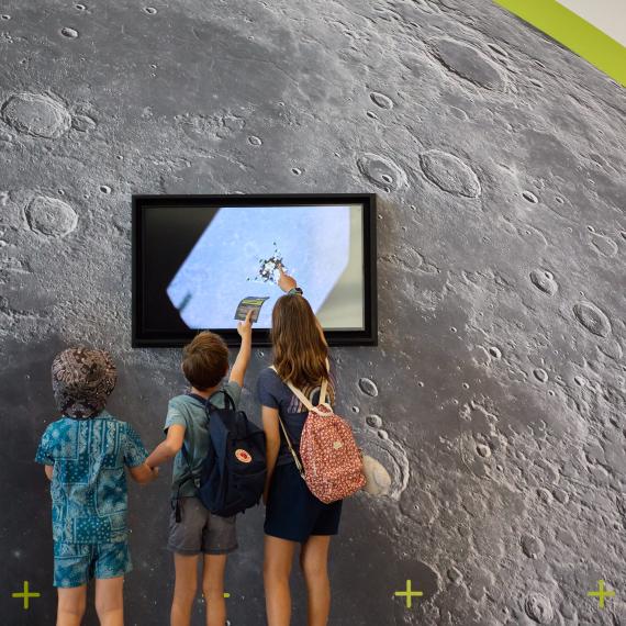 3 children stand in front a screen with moon images on it. 