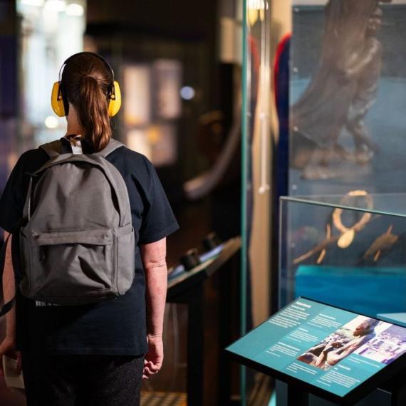A woman wearing headphones examines a display of artifacts, immersing herself in the rich history they represent.