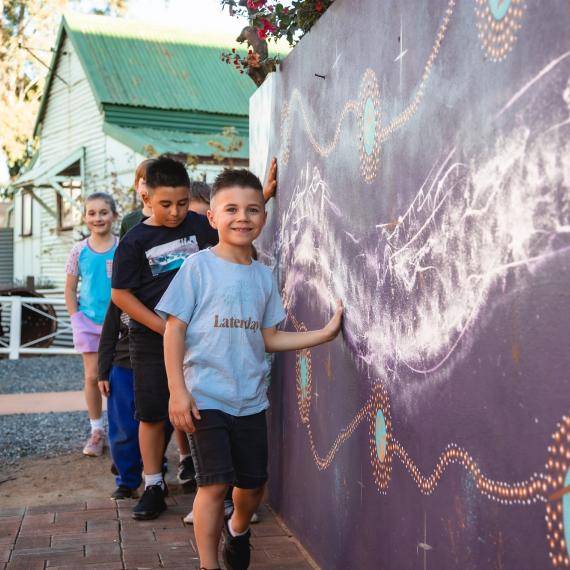 a group of young children with happy expressions and they are walking alongside a wall painted with using purples oranges and white colours 