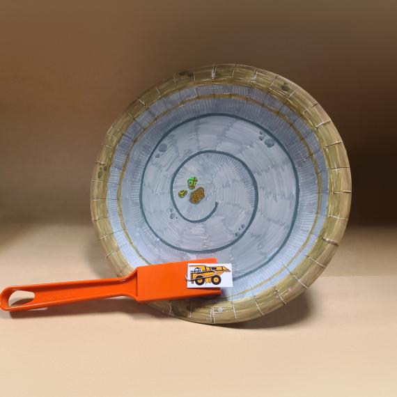 a decorated paper plate with a swirl pattern and an orange paddle sitting on the plate with a small picture of a mine truck clipped to the top of the paddle