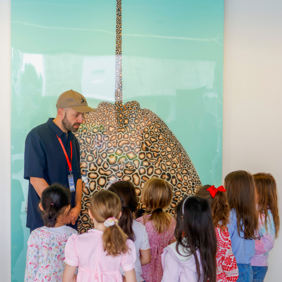 Artist Ian Daniell stands in front of a colourful artwork with a group of children