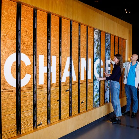 Two people interact with a wooden panel displaying the word "CHANGES" in large white letters.