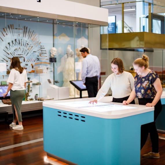 Visitors interact with exhibits in a modern museum, including digital tables and display cases.